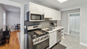 Una cocina compacta con armarios blancos, estufa de acero inoxidable, microondas y lavavajillas.