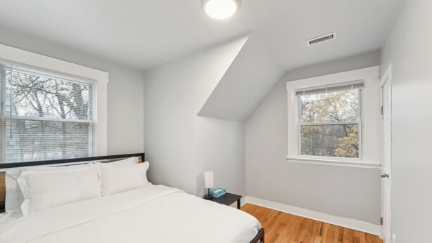 A bedroom with a bed, a nightstand, a window, and a door.