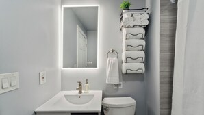 Un baño moderno con un lavamanos blanco, un espejo, un inodoro y un toallero con toallas dobladas con esmero.