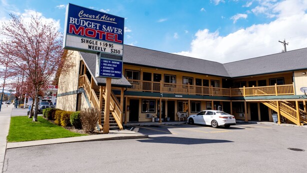 A motel with a sign advertising budget-friendly rates, a covered parking area, and a two-story building with a balcony. - Coeur D'Alene Budget Saver (Coeur d'Alene)