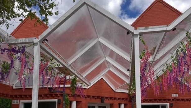 Un patio couvert, avec une façade en briques rouges, des colonnes blanches et des fleurs violettes suspendues.