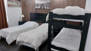 Une chambre avec deux lits superposés, une tête de lit en bois, une table de chevet avec une lampe et un tableau encadré au mur.