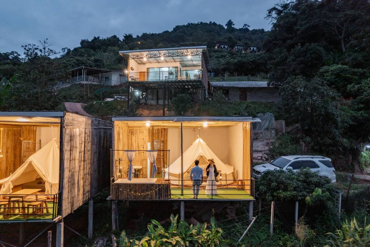 A series of wooden cabins with attached tents, each featuring a balcony and a small outdoor seating area.