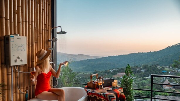 A woman in a red dress sitting in a bathtub with a showerhead above, overlooking a mountainous landscape. - Mankhao Homestay (Mae Rim)