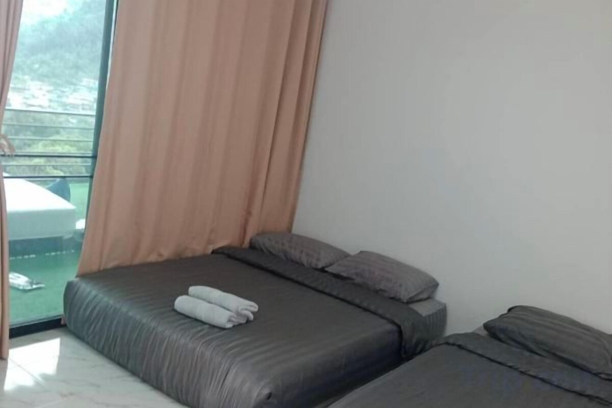 A room with two beds, a window with curtains, and a view of greenery outside.