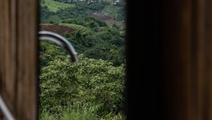 A view from a window with a metal railing, overlooking a lush green landscape with rolling hills and a misty valley. - Mankhao Homestay (Mae Rim)