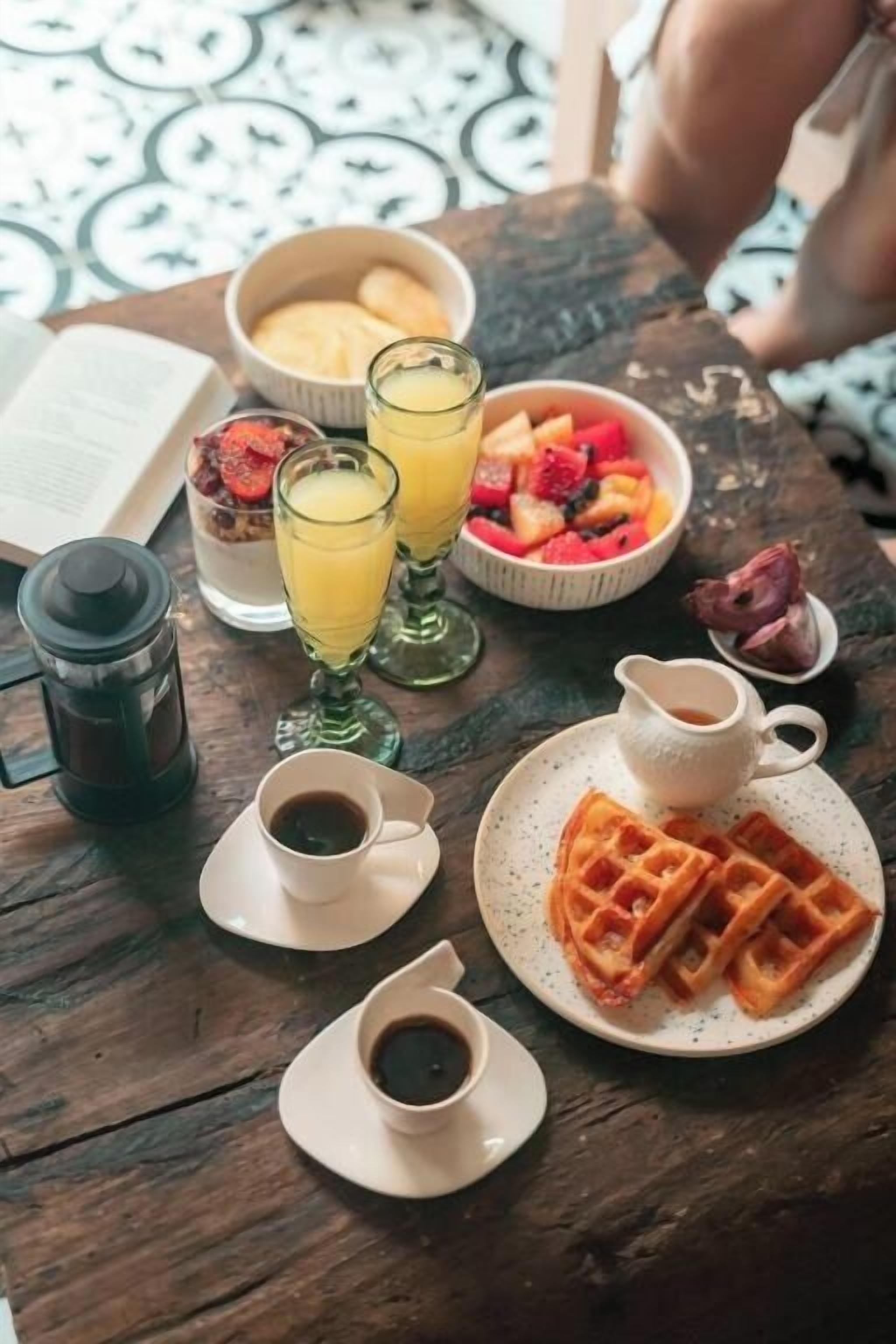 Et morgenbord med vafler, frugt, juice og kaffe.