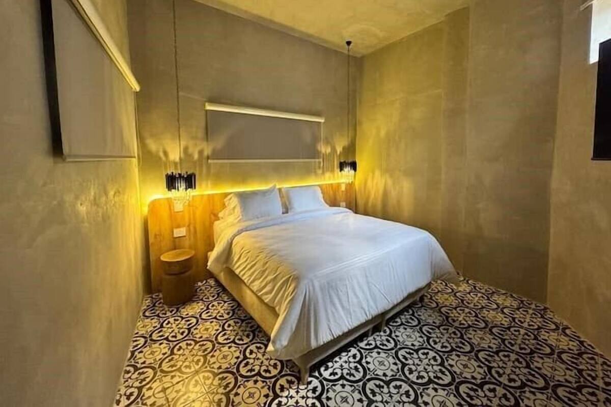 Un dormitorio con cama, una mesita de noche, un aplique de pared y baldosas estampadas.