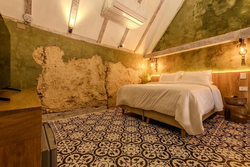 Ein Schlafzimmer mit Bett, gemustertem Boden, freiliegenden Backsteinwänden und Holzbalken.