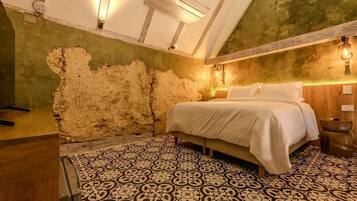 Ein Schlafzimmer mit Bett, gemustertem Boden, freiliegenden Backsteinwänden und Holzbalken.