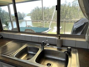 Una cocina con dos lavamanos de acero inoxidable, una ventana con vista a un cuerpo de agua y árboles, además de un muelle.