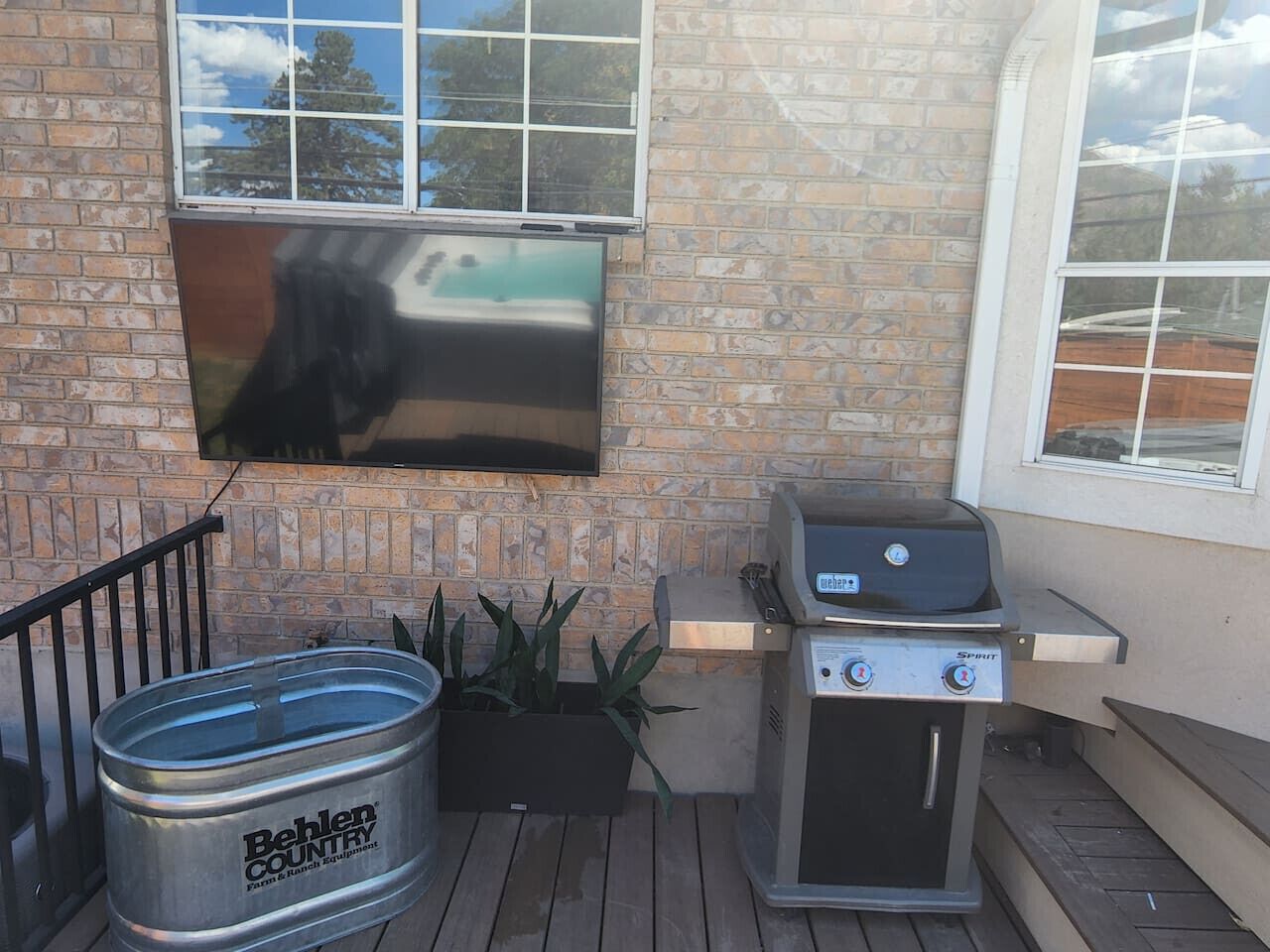 A brick exterior with a flat-screen TV mounted on the wall, a barbecue grill, and a metal barrel labeled "Behlens Country Store."
