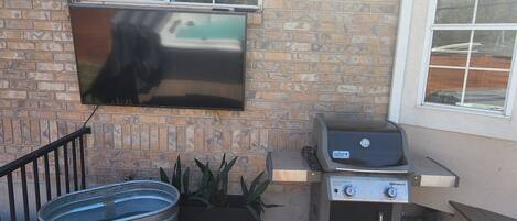 A brick exterior with a flat-screen TV mounted on the wall, a barbecue grill, and a metal barrel labeled "Behlens Country Store."