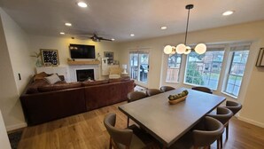 Un salon moderne avec une cheminée, un coin repas avec une table et des chaises, et une grande fenêtre laissant entrer la lumière naturelle.