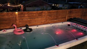 Un bain à remous avec une terrasse en bois, un flotteur en forme de flamant rose et des lumières rouges.