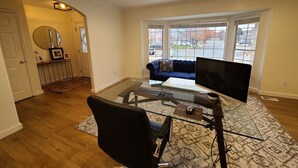 Un salon avec un bureau en verre, un fauteuil de bureau noir, un canapé bleu et une grande fenêtre donnant sur la rue.