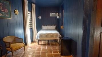 Ein Zimmer mit einem Bett, einem Sessel, einem kleinen Tisch und einer Wand-Klimaanlage.