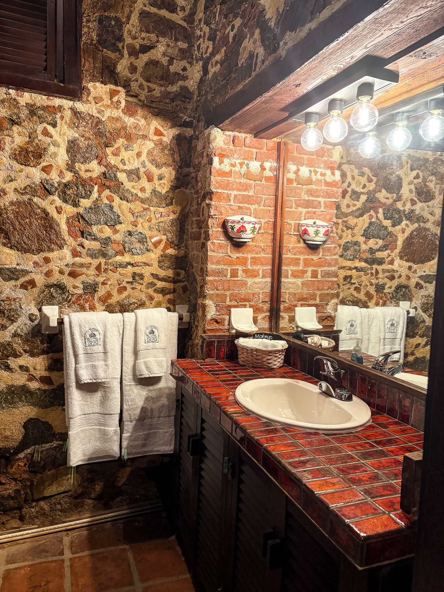 A bathroom with a stone wall, a large mirror, and a sink.