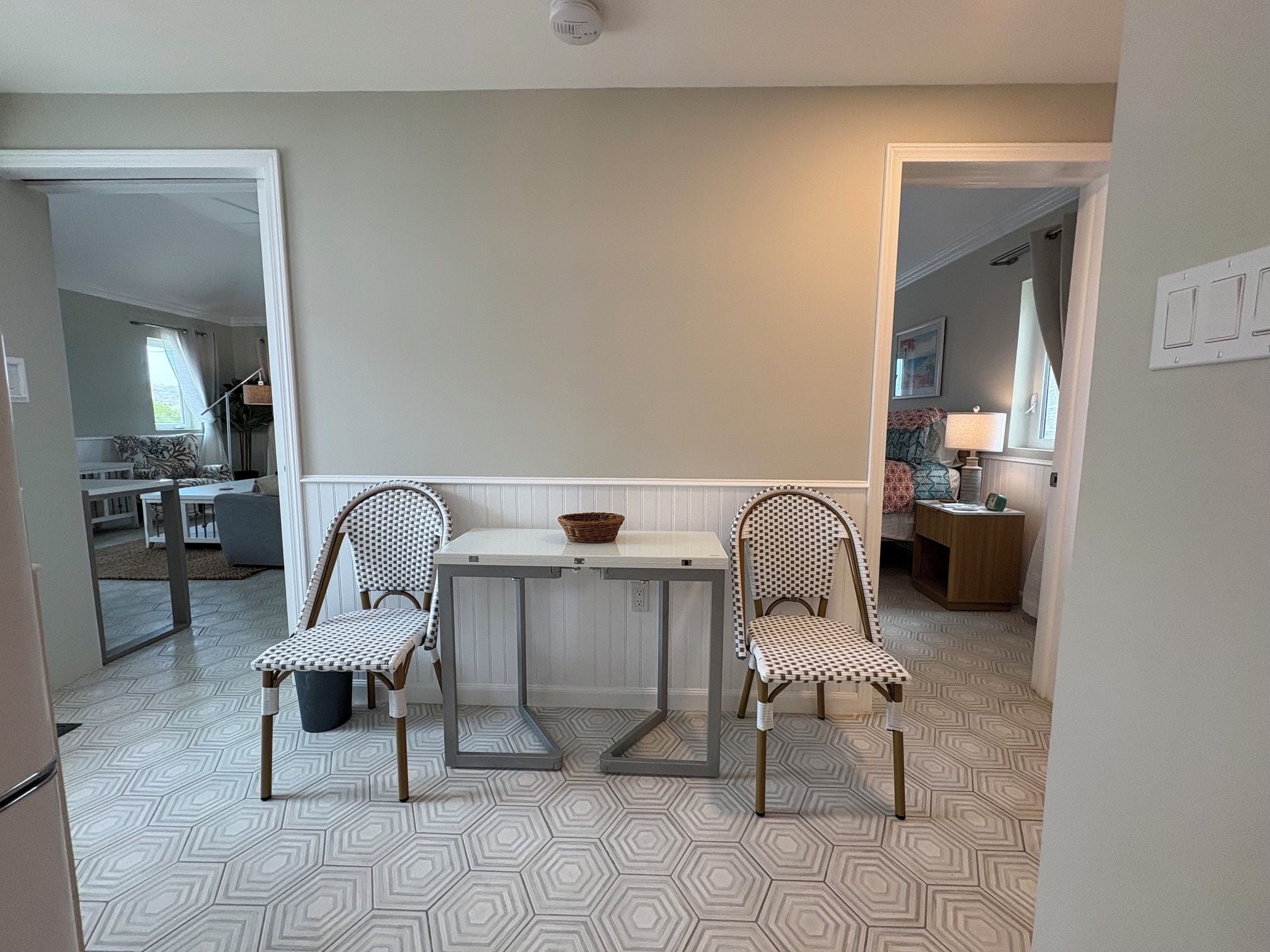 A dining area with a table and two chairs, a window with a view, and a patterned floor.