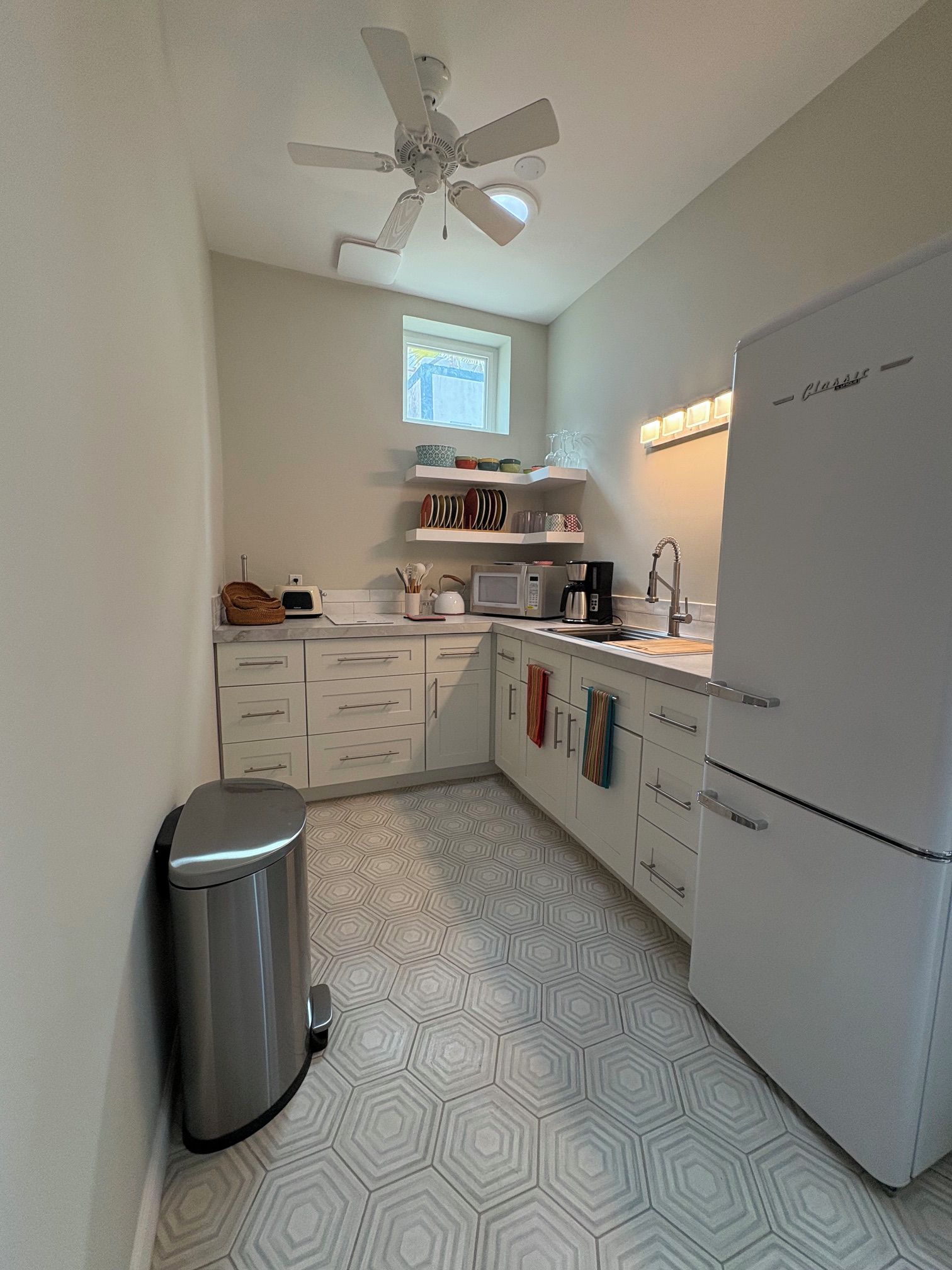 Una cocina compacta con microondas integrado, refrigerador y ventilador de techo.