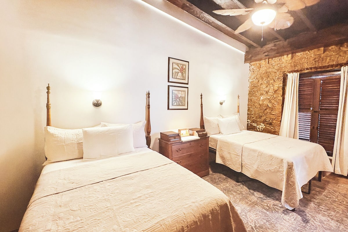 Una habitación con dos camas, cabecero de madera, pared de piedra y ventilador de techo.