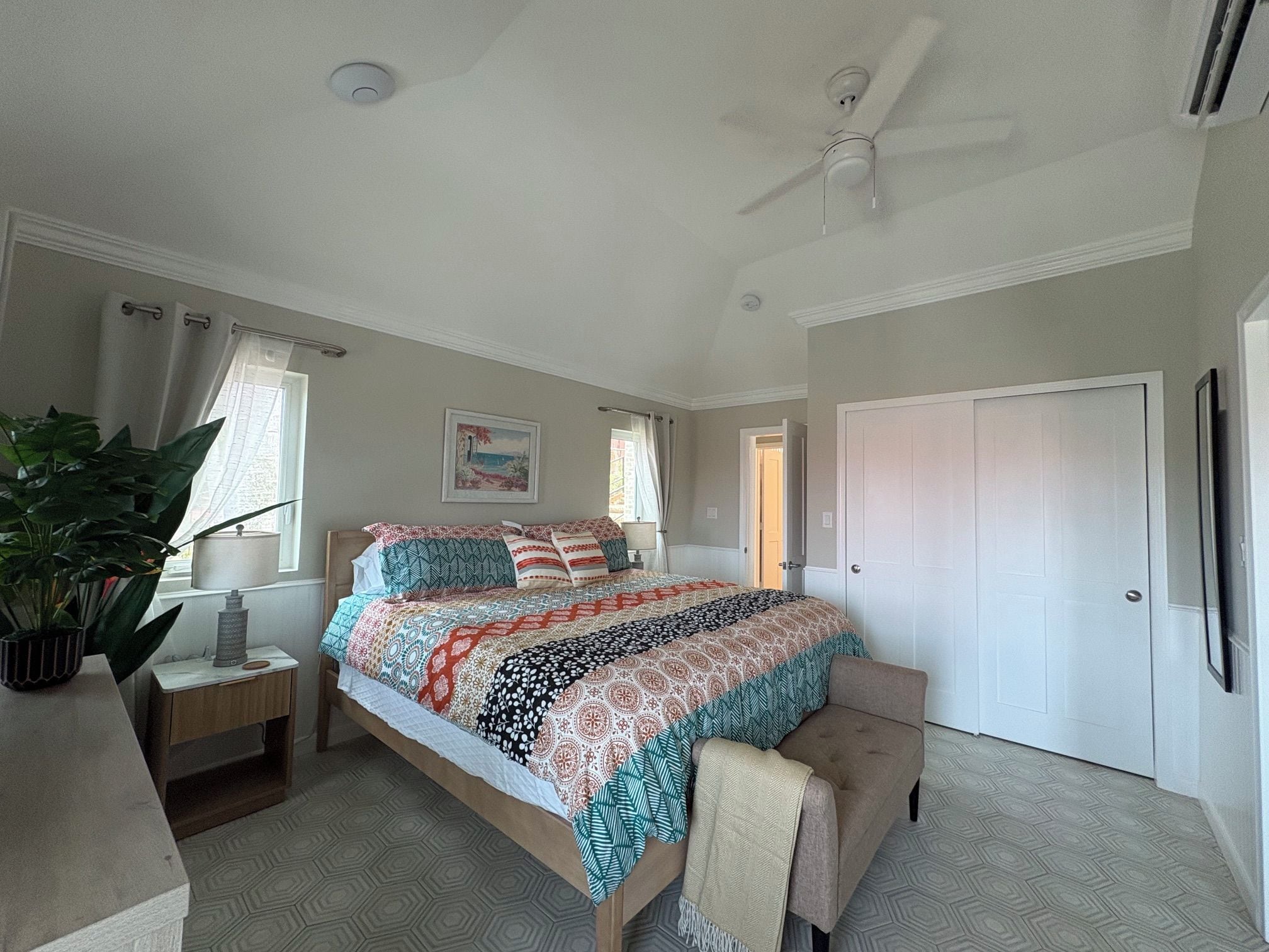 A bedroom with a bed, a ceiling fan, a door, and a window with curtains.