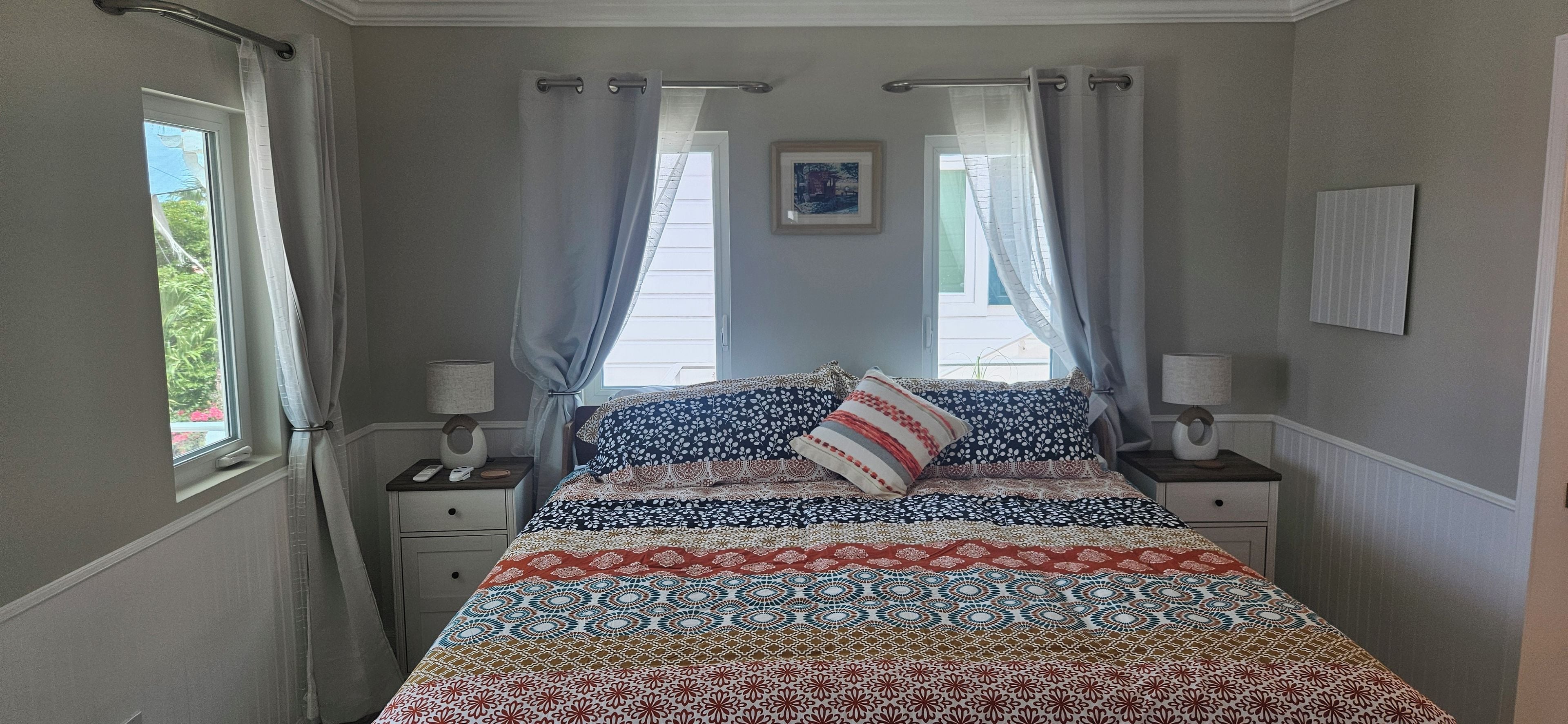 A bedroom with a bed, two bedside tables, a window with curtains, and a wall-mounted picture.