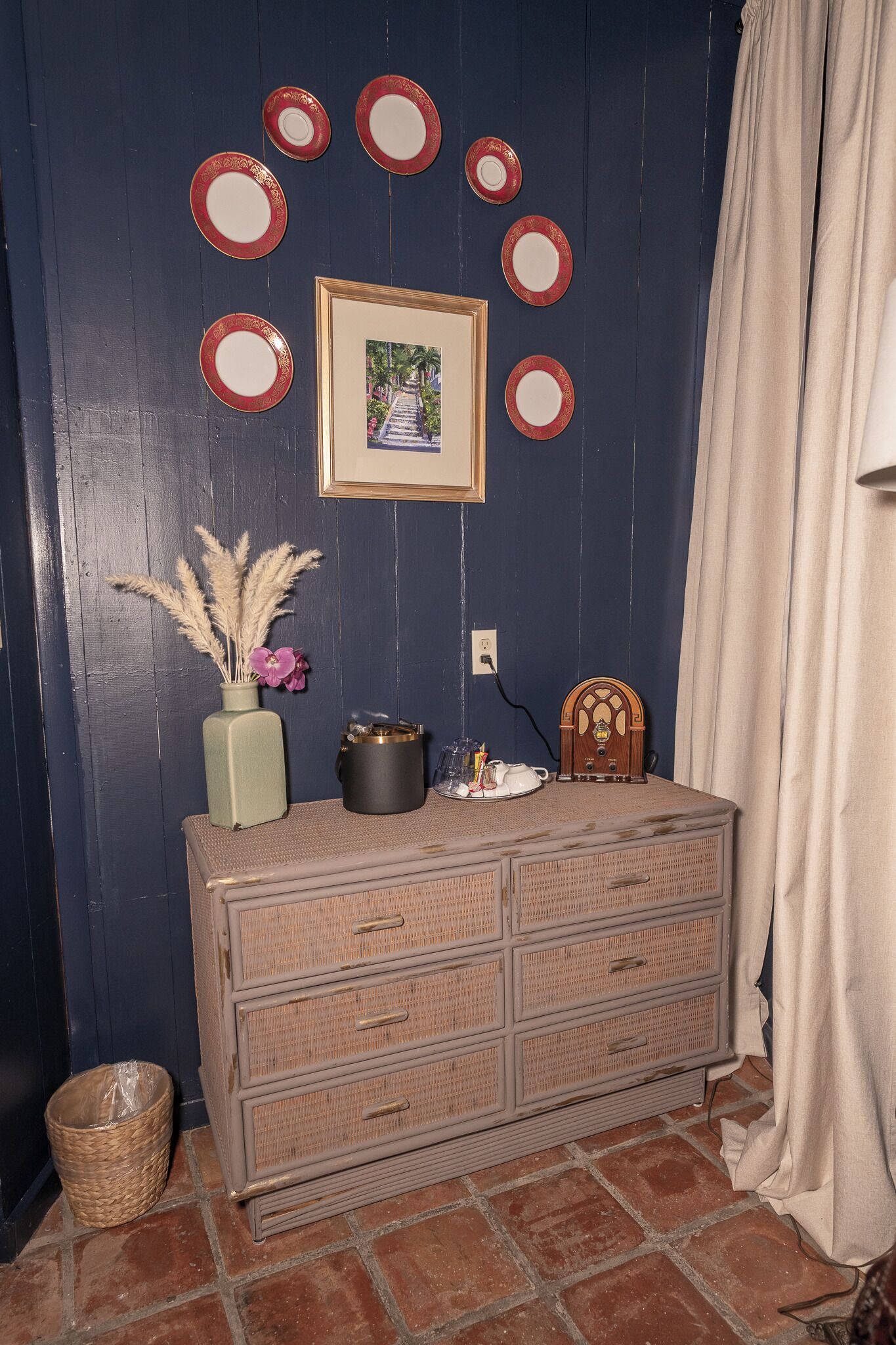 A room with a dresser, a vase with dried plants, a framed picture, and a wall with circular decorations.