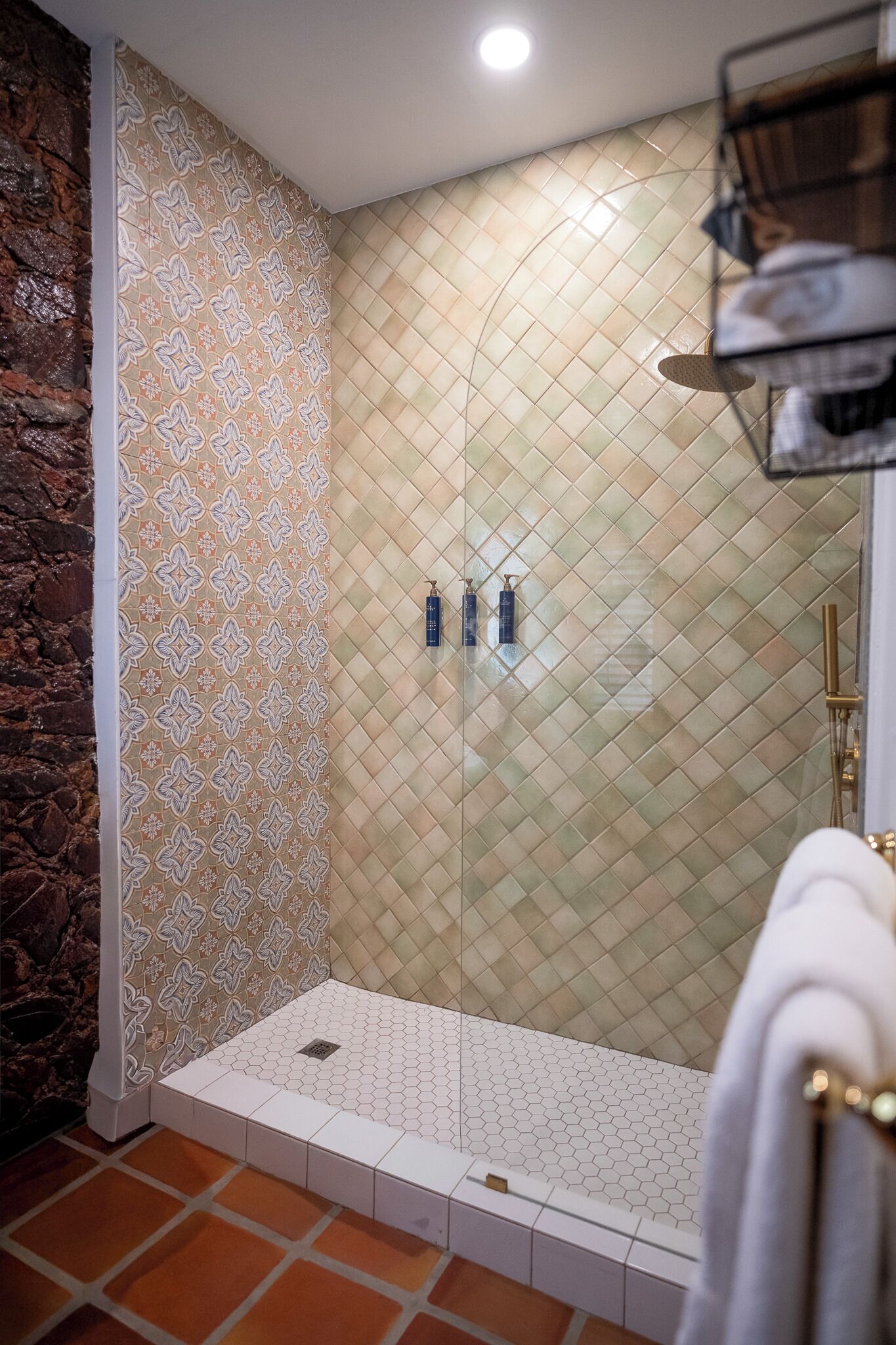 Ducha con pared con estampado, suelo de azulejos y repisa con toallas.
