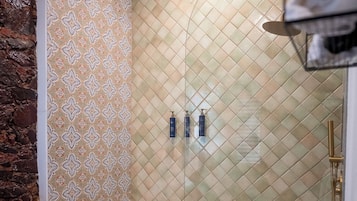 Ducha con pared con estampado, suelo de azulejos y repisa con toallas.