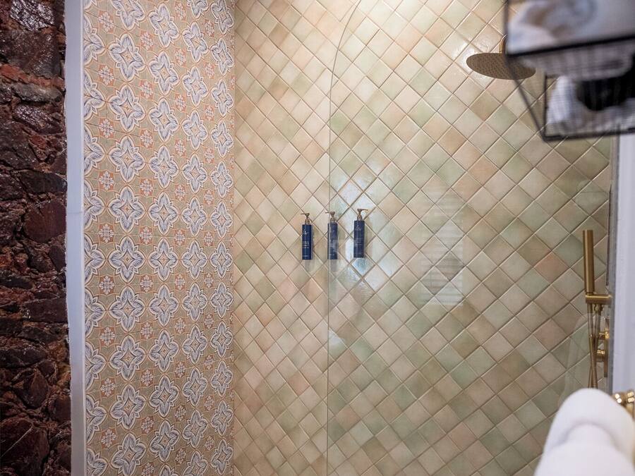 Ducha con pared con estampado, suelo de azulejos y repisa con toallas.