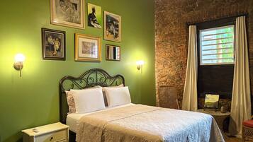 Un dormitorio con cama, luces empotradas en la pared, cuadros enmarcados, una ventana con cortinas y una pared de piedra.
