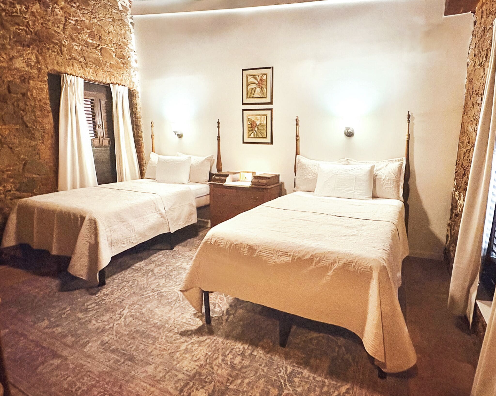 Una habitación con dos camas, una mesita de noche, una lámpara fijada a la pared y un cuadro enmarcado.