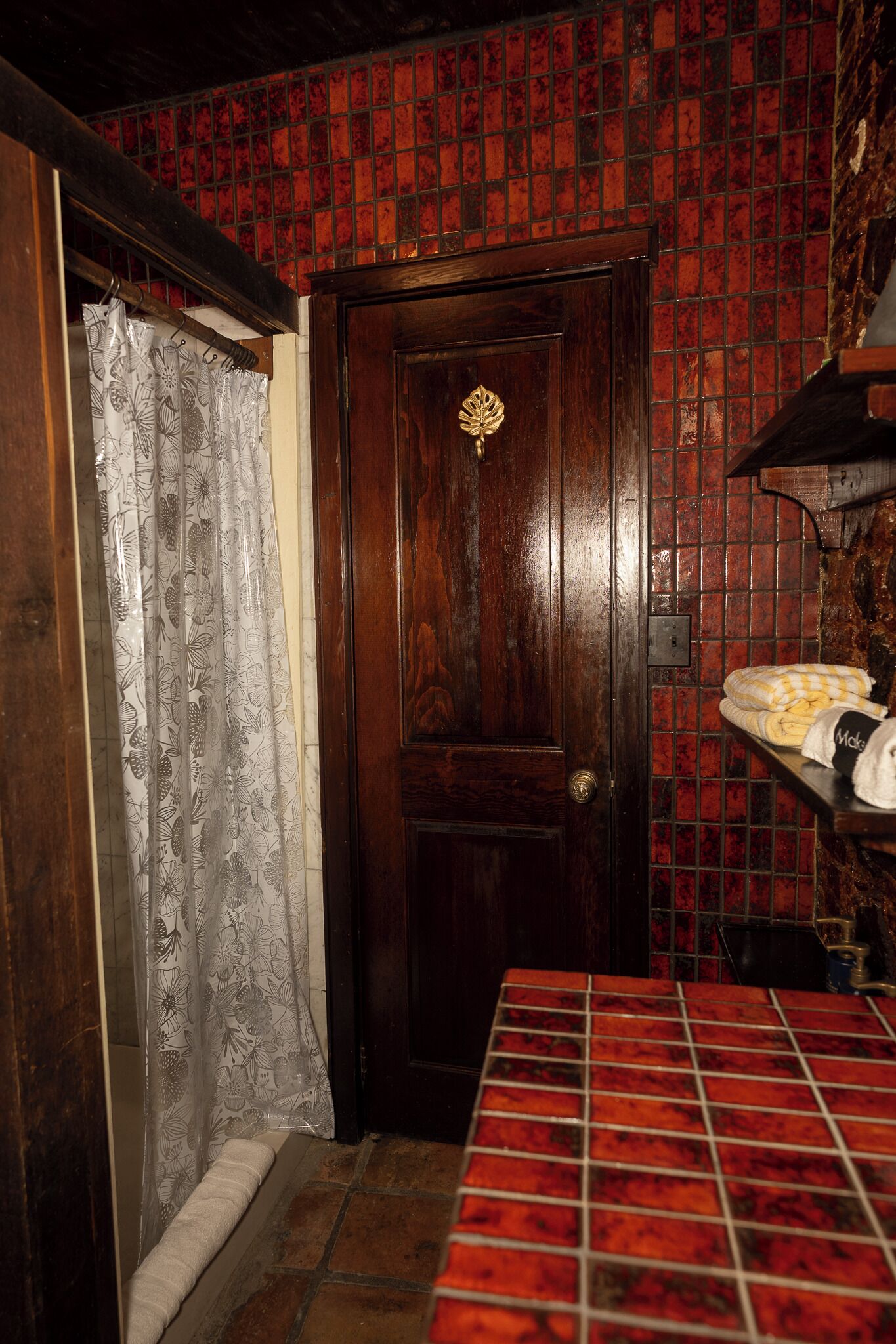 Een badkamer met een houten deur, betegelde wanden, een douchegordijn en een handdoekhouder.
