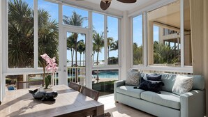 A sunlit room with large windows, a pool view, a light blue sofa, and a dining table with chairs. - Sunrise Retreat: Ocean & Pool Views, Gym, PB Courts, Game Room, Marina and more (Key Largo)