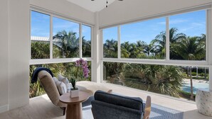 A spacious room with large windows offering a view of palm trees and a pool. - Sunrise Retreat: Ocean & Pool Views, Gym, PB Courts, Game Room, Marina and more (Key Largo)
