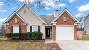 A two-story house with a brick facade, a white garage door, and a small front yard with a brick pathway.
