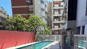 A swimming pool with a glass railing, a red wall, and a modern building in the background.