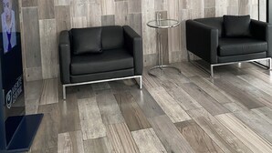 A modern room with a herringbone-patterned wood wall, two black leather sofas, a small round table, and a poster on the left.