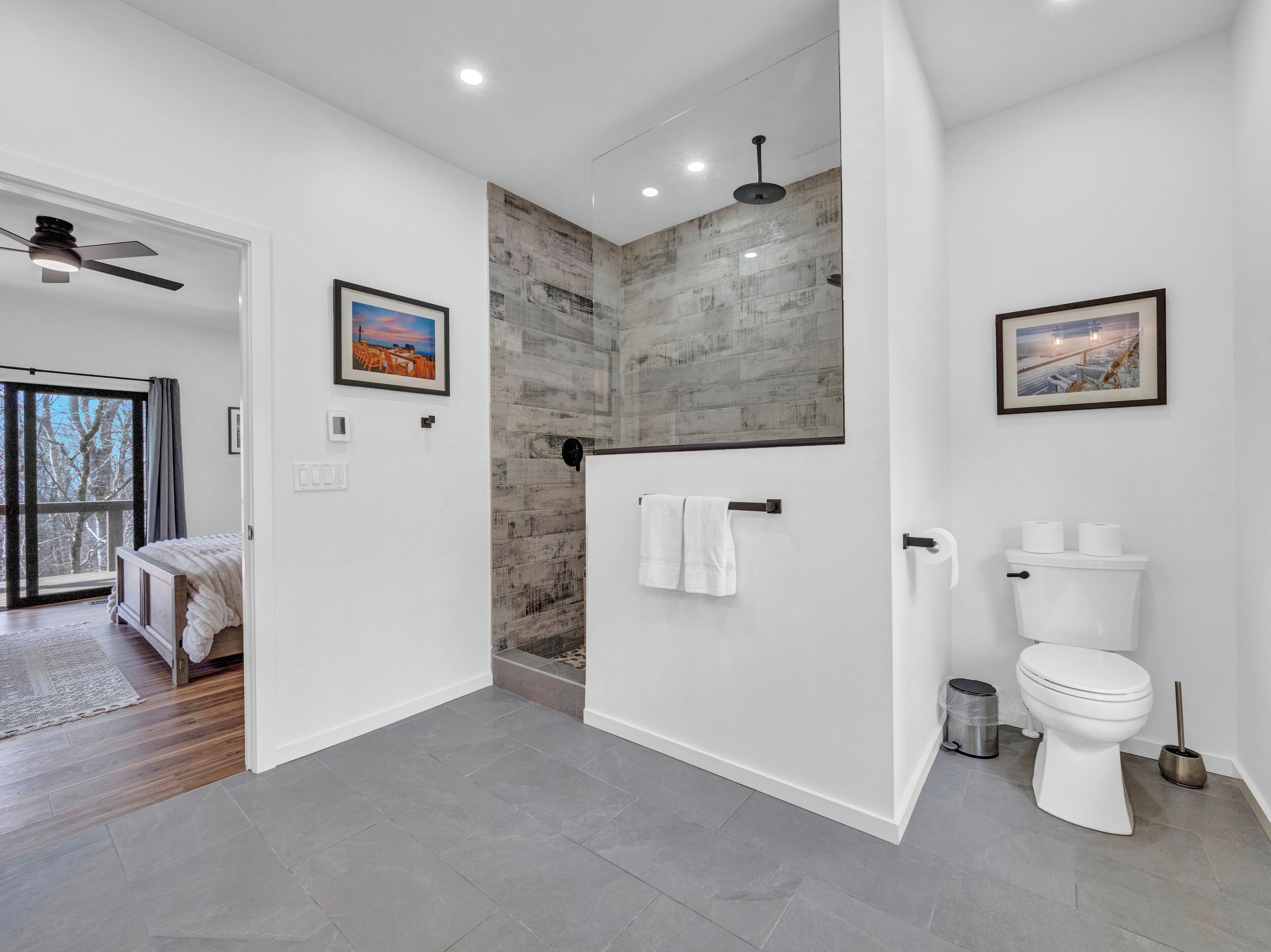 A modern bathroom with a shower, toilet, and a large window.