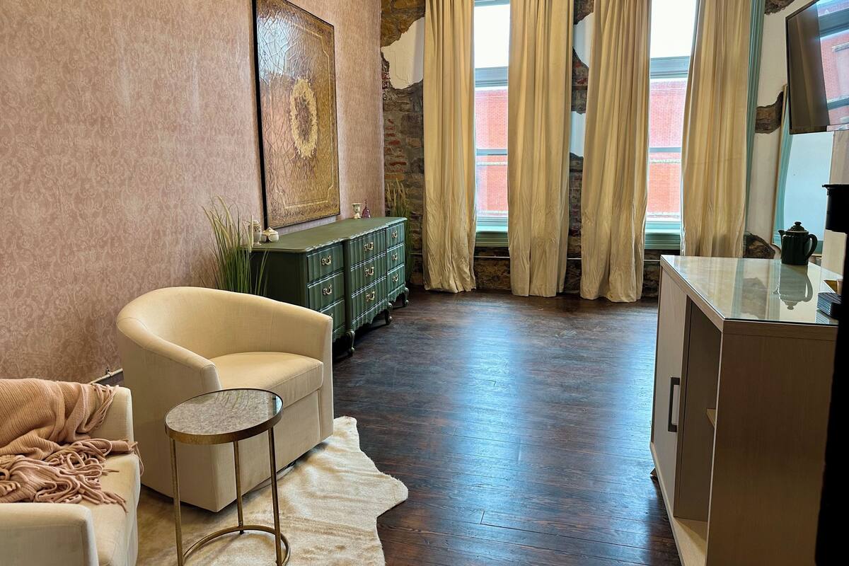 A room with a stone wall, a green dresser, a beige armchair, a small round table, and a white rug.