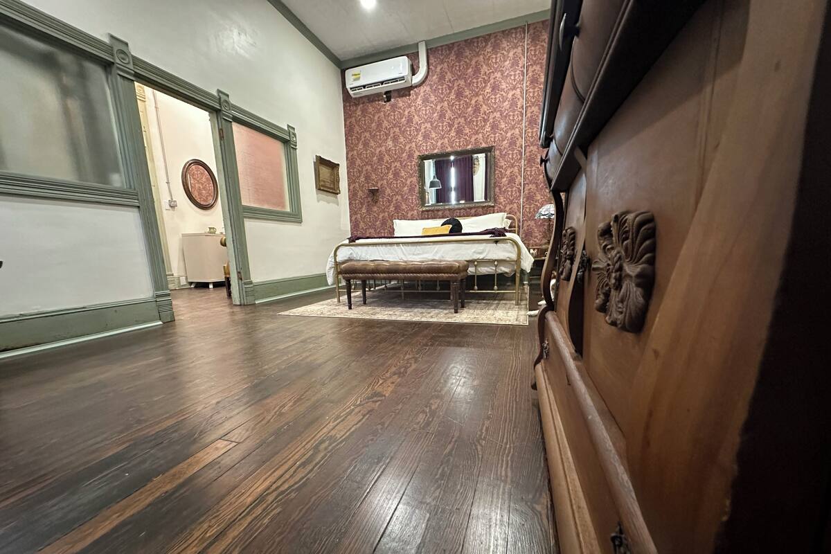 A room with a bed, a bench, a dresser, and an air conditioning unit on the wall.