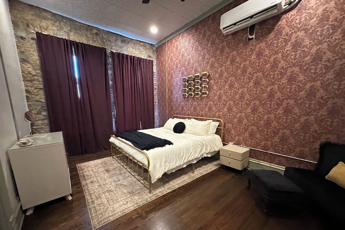A bedroom with a bed, a nightstand, a dresser, a rug, and a wall-mounted air conditioner.