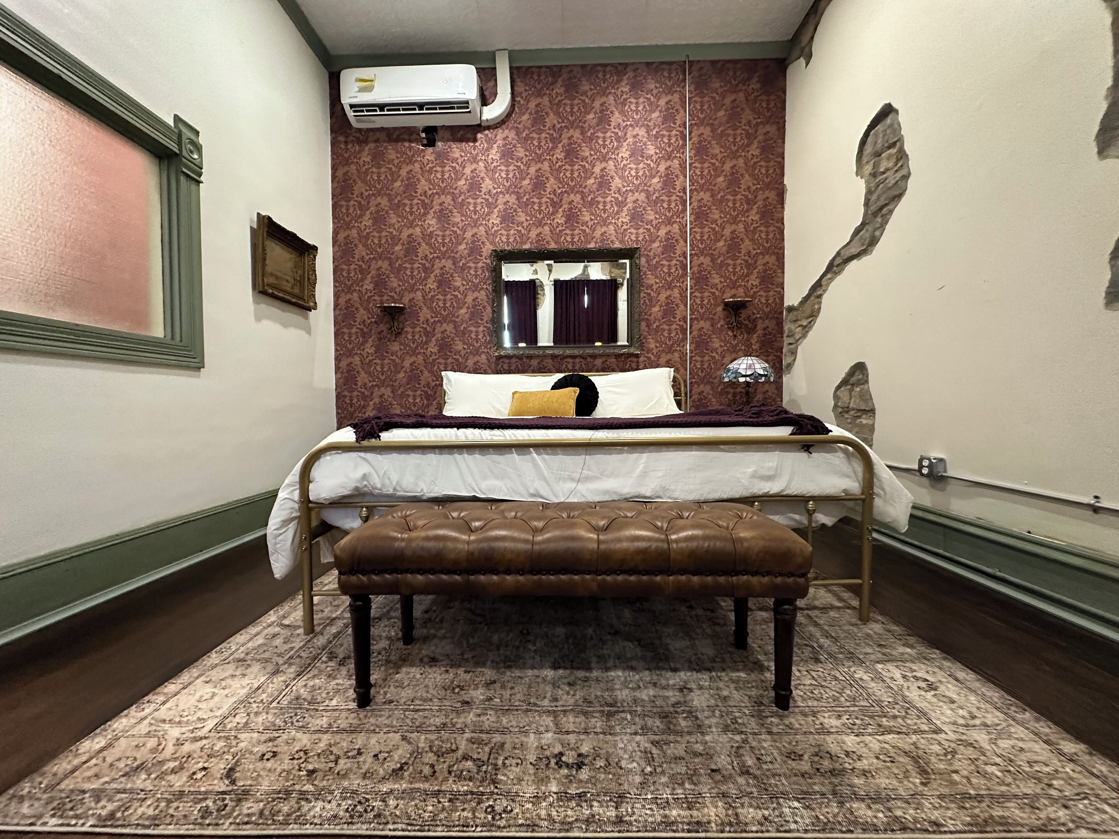 Ein Schlafzimmer mit einem Bett, einer Bank, einem Spiegel und einer Klimaanlage.