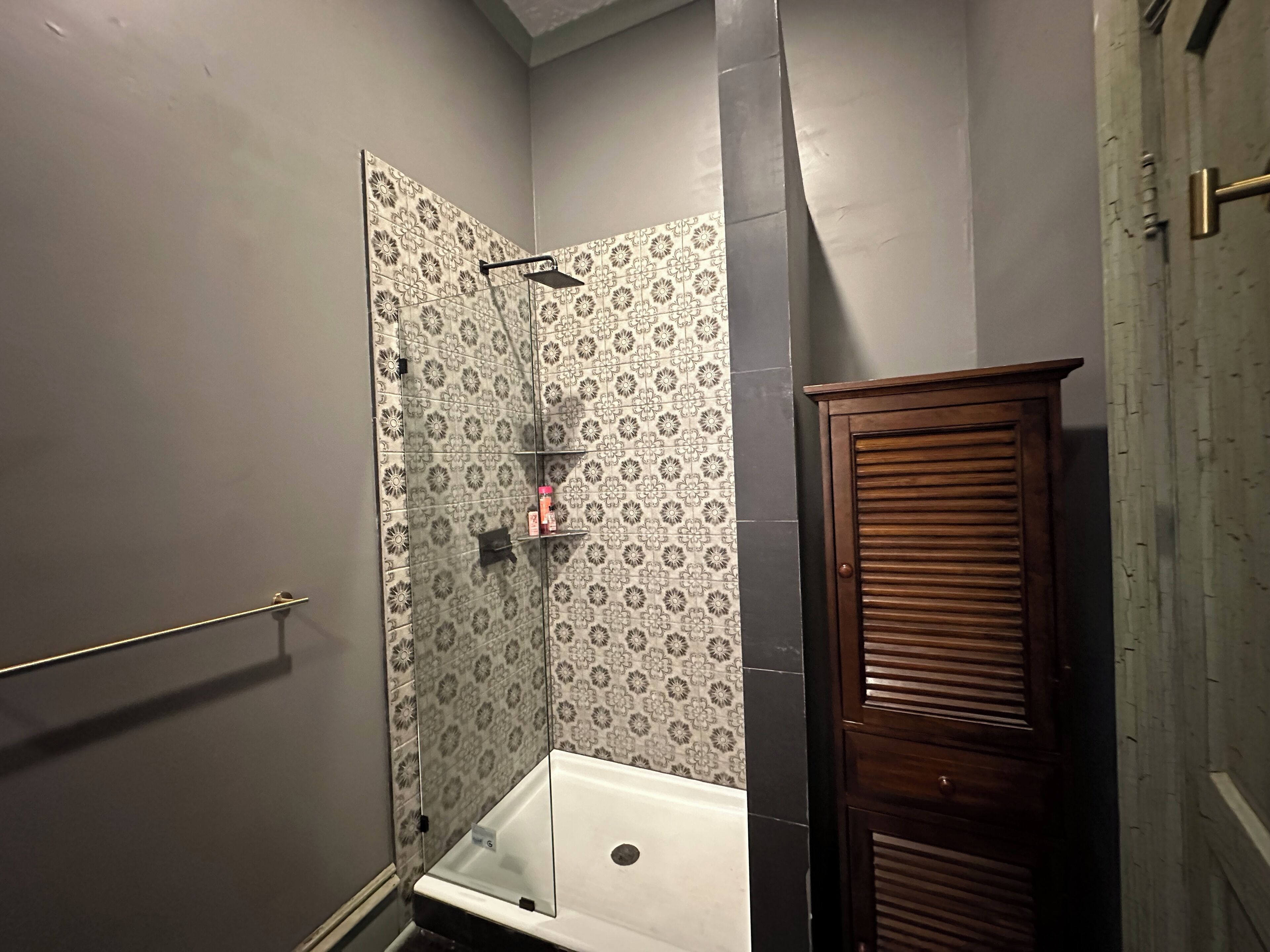 A bathroom with a shower, a toilet, and a wooden cabinet.