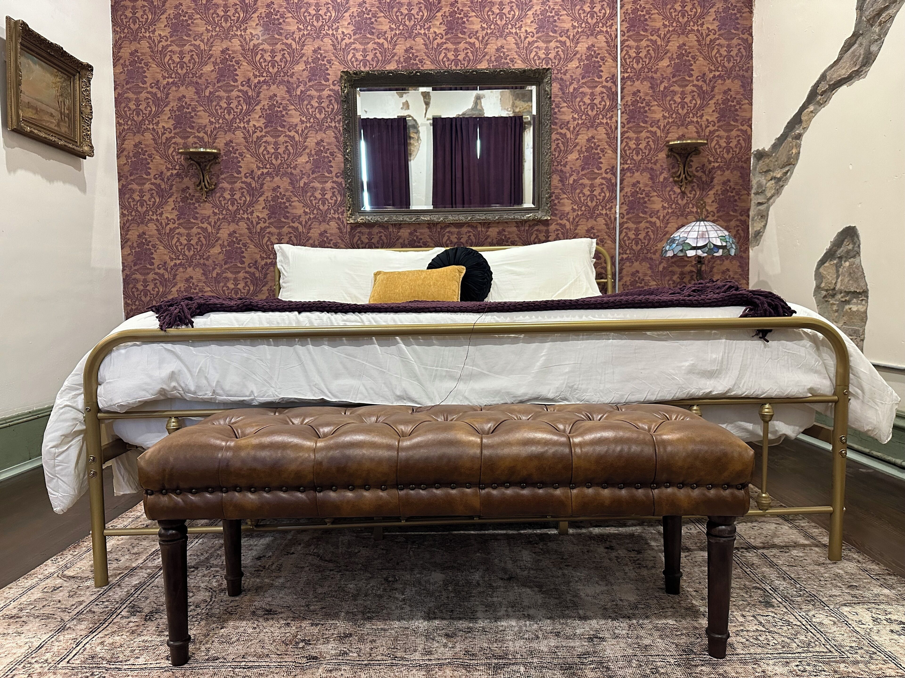 Un dormitorio con cama, un banco, una ventana con cortinas y una pared con diseño decorativo.