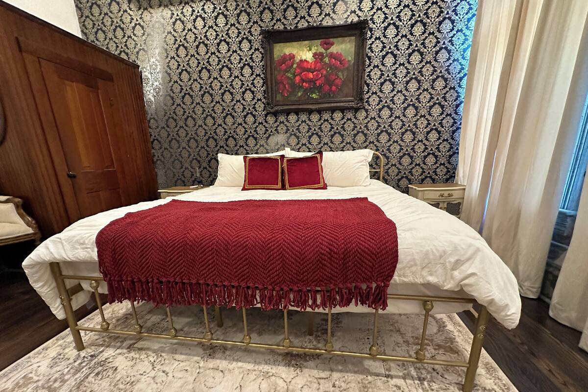 A neatly made bed with a red blanket, a wooden wardrobe, a nightstand, and a framed picture on the wall.