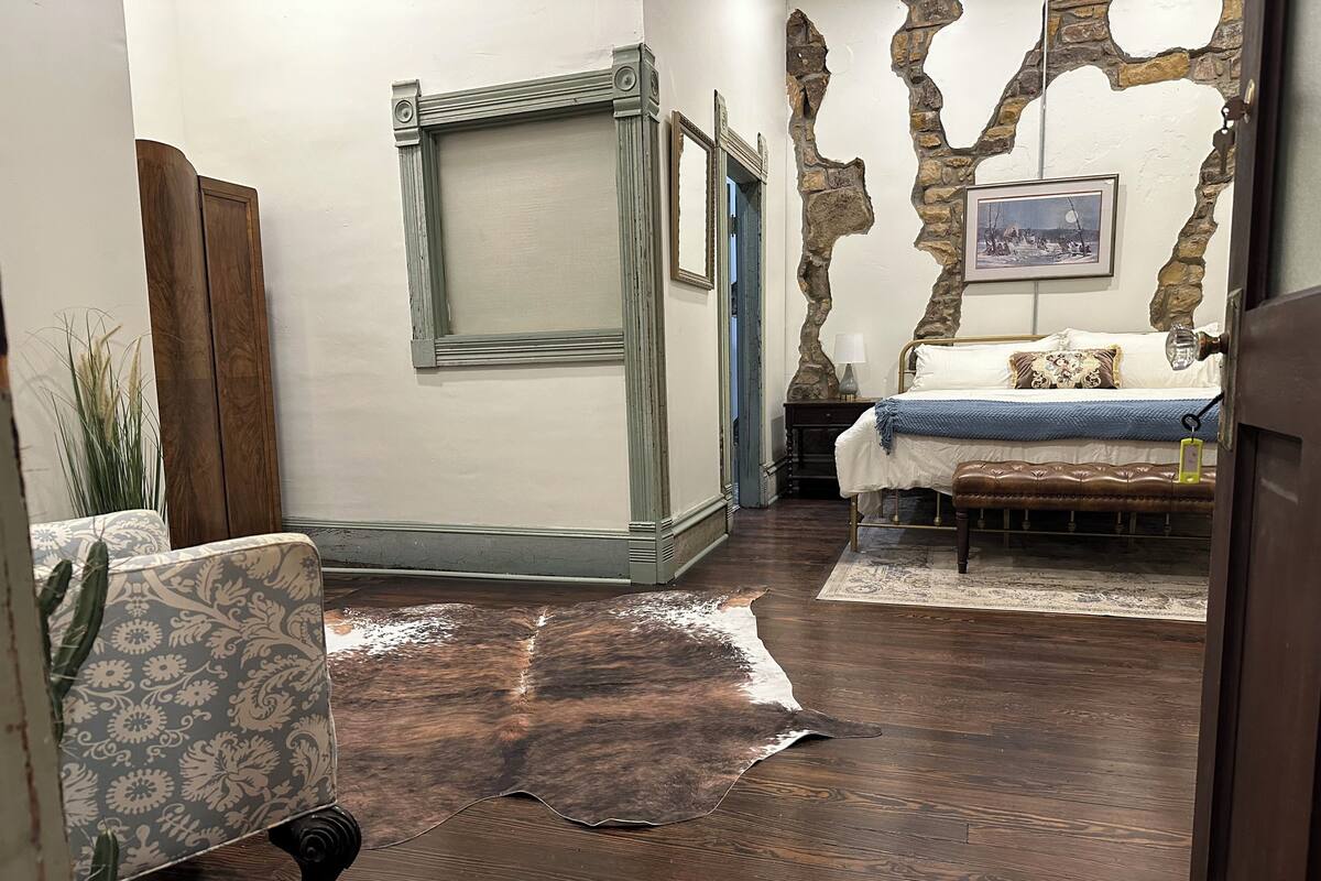 A room with a bed, a chair, a rug, and a stone wall.