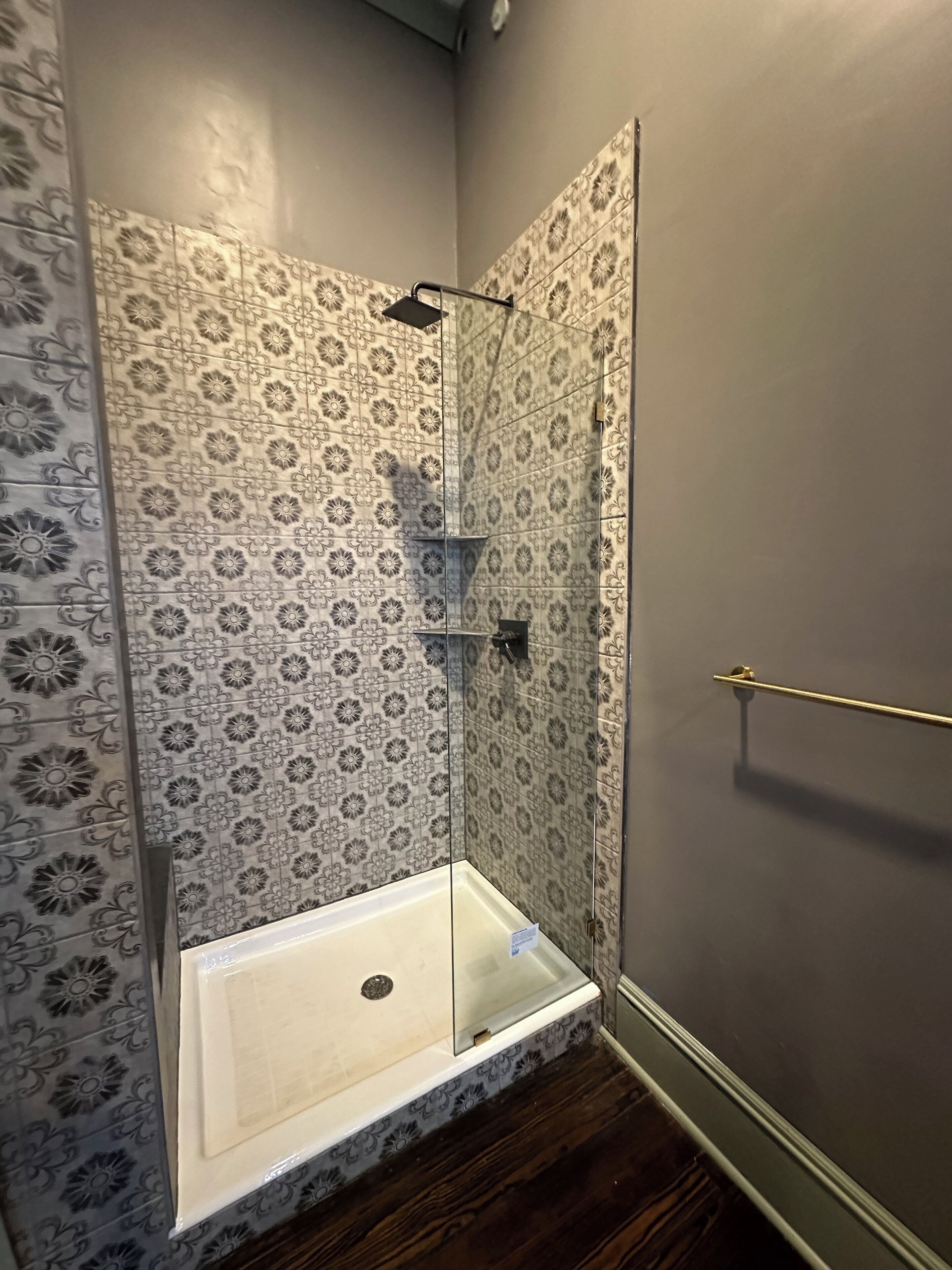A shower with a glass door, a metal towel rack, and patterned tiles on the walls.