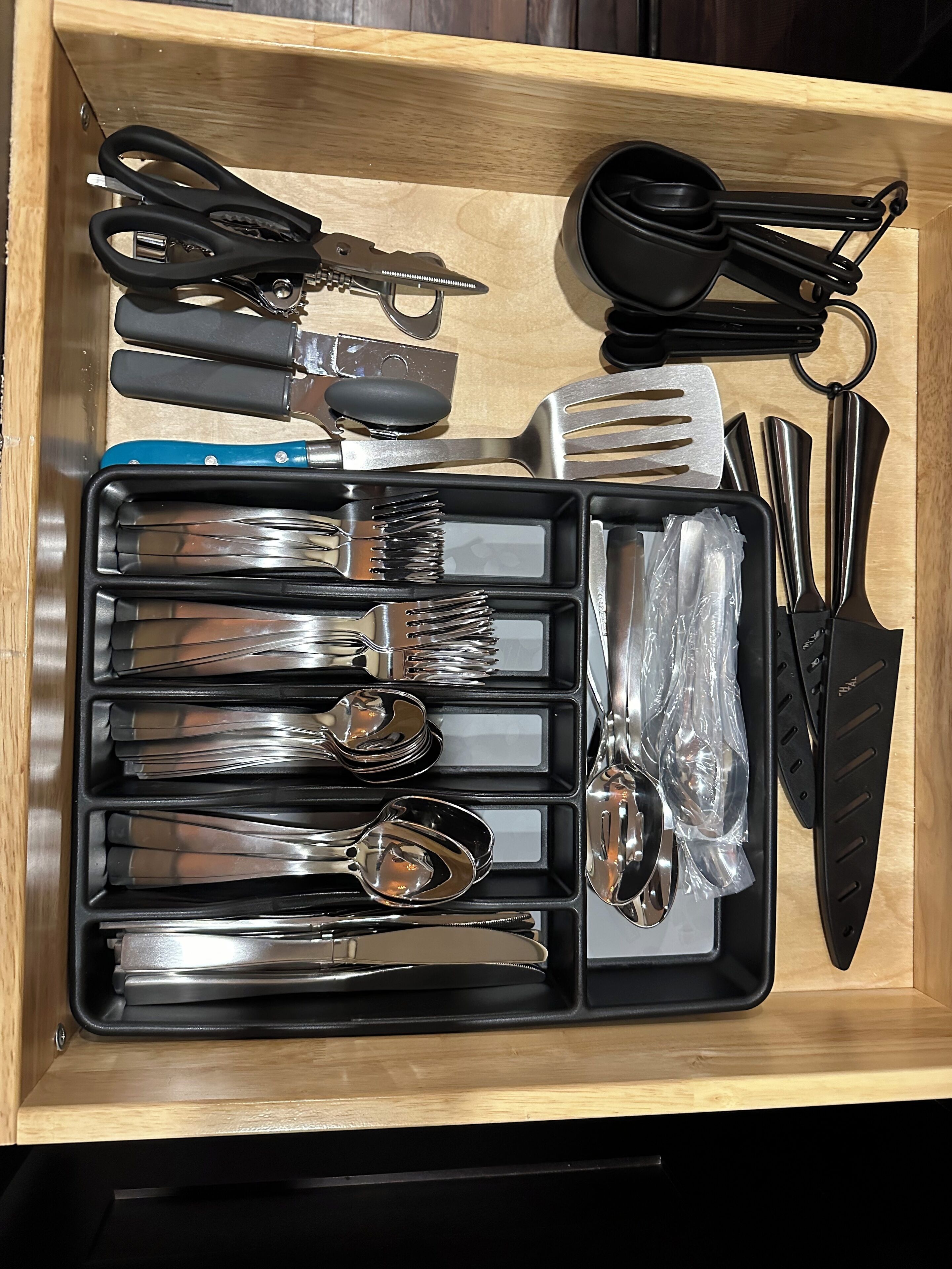 A drawer containing various kitchen utensils including a knife, spoon, fork, and scissors.